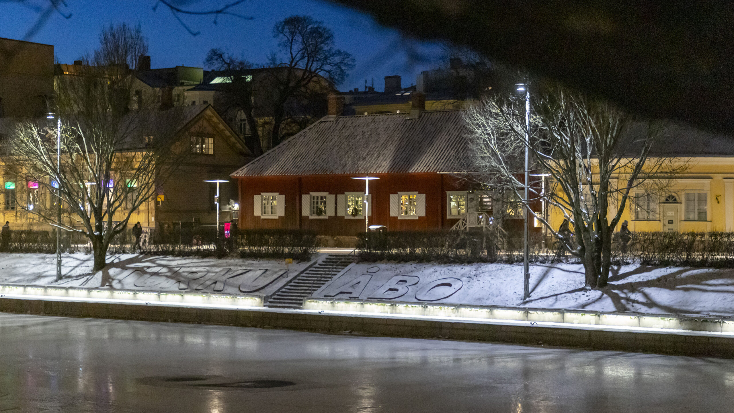 Tunnelmallinen talvi-ilta Aurajoen rannassa, vastarannassa museon punainen puurakennus.